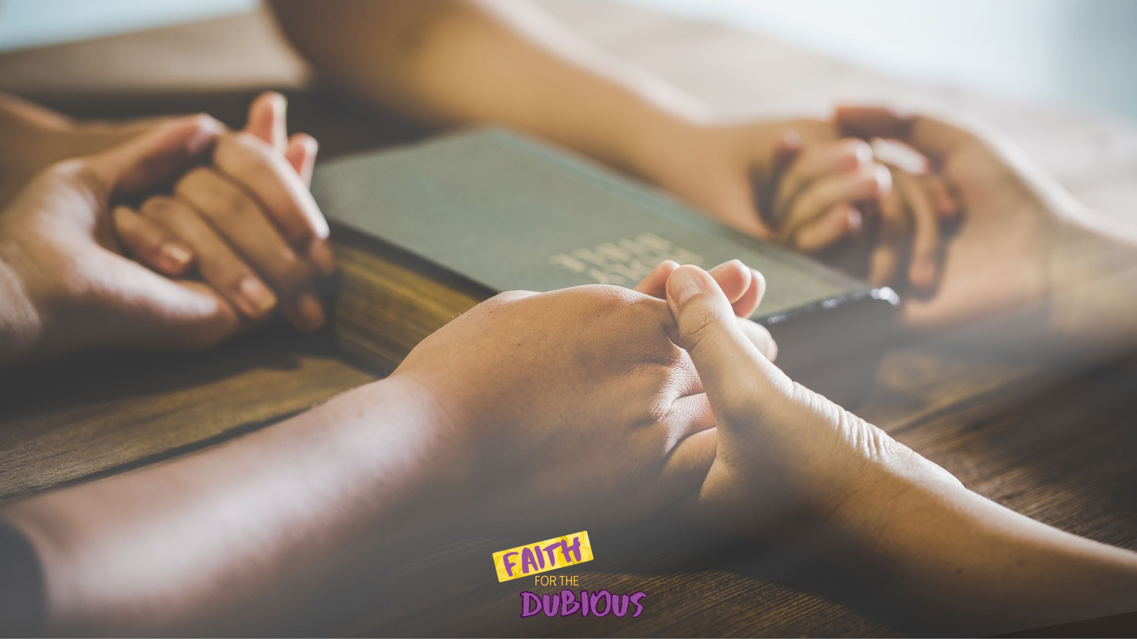 Friends holding hands and praying over Bible verses on the Power of Prayer with a bible in between them.