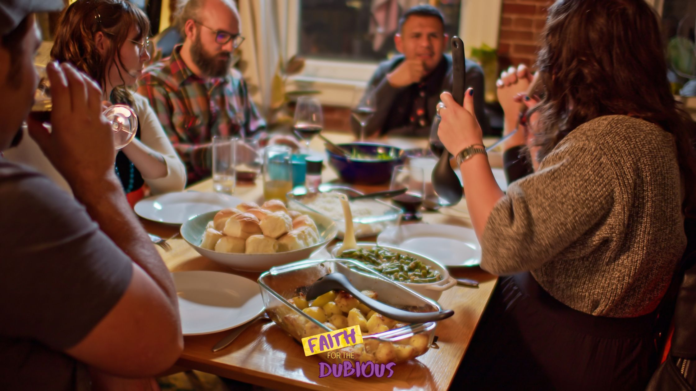 People sitting around a table with food depicting how church is a pot luck.