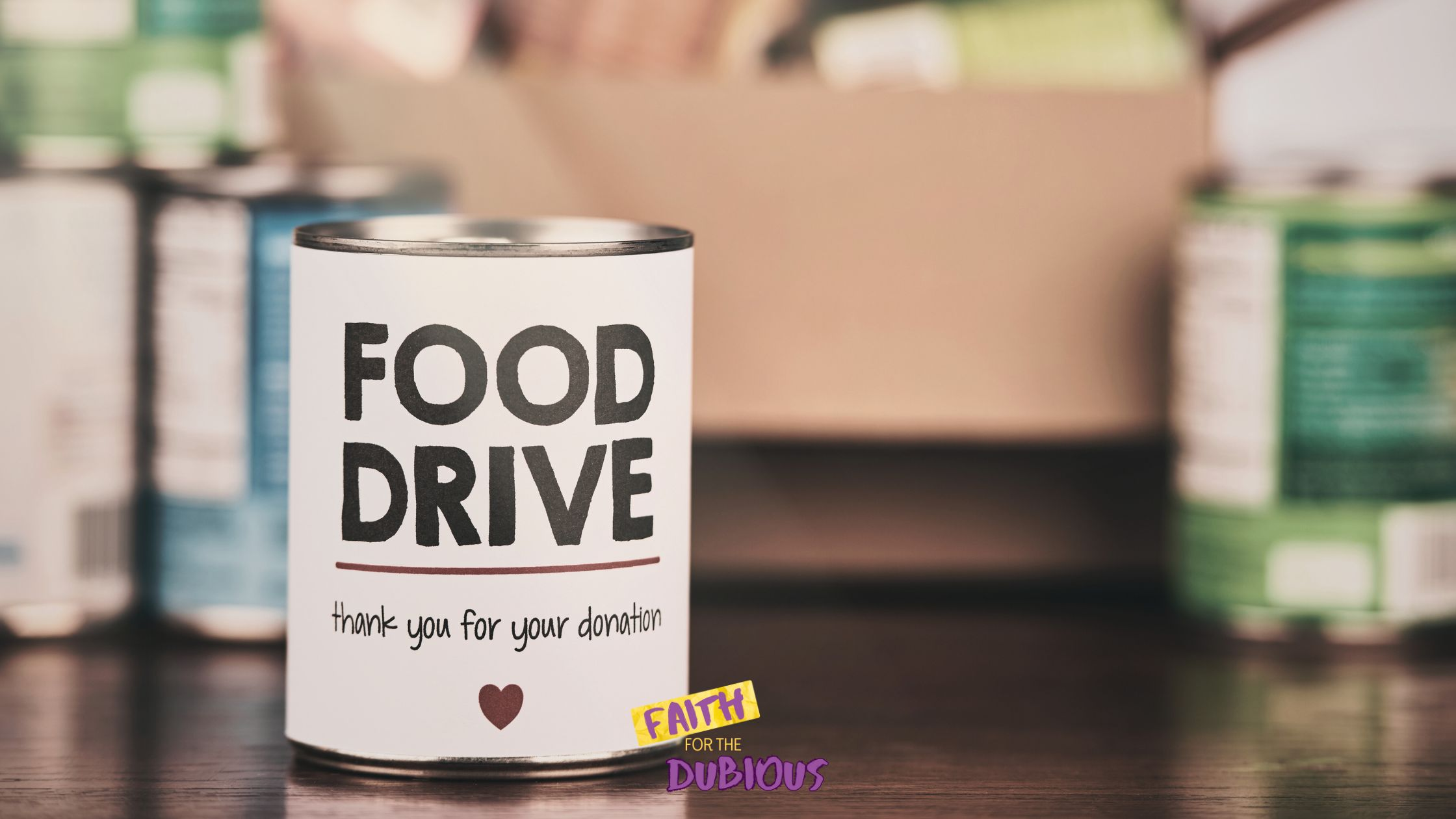 A box of food from a canned food drive with a can in front reading "Food Drive"